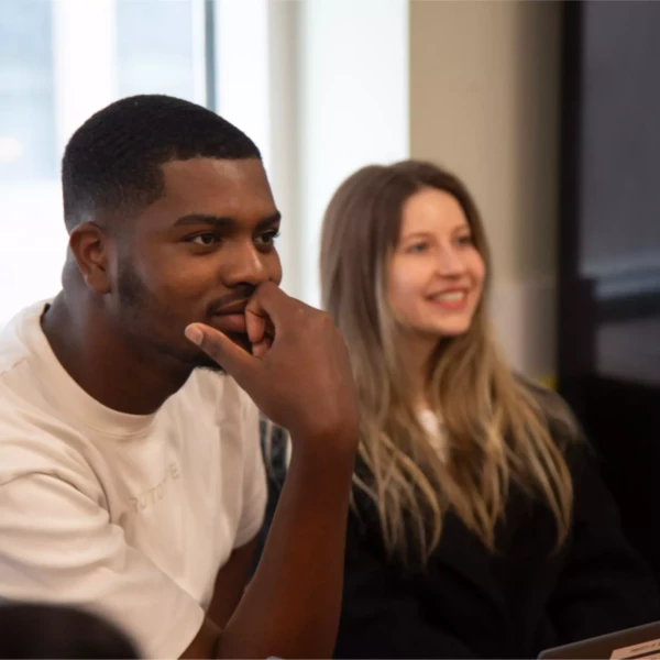 Diverse group of people engaged in a meeting, smiling and attentive, near a window with natural light.