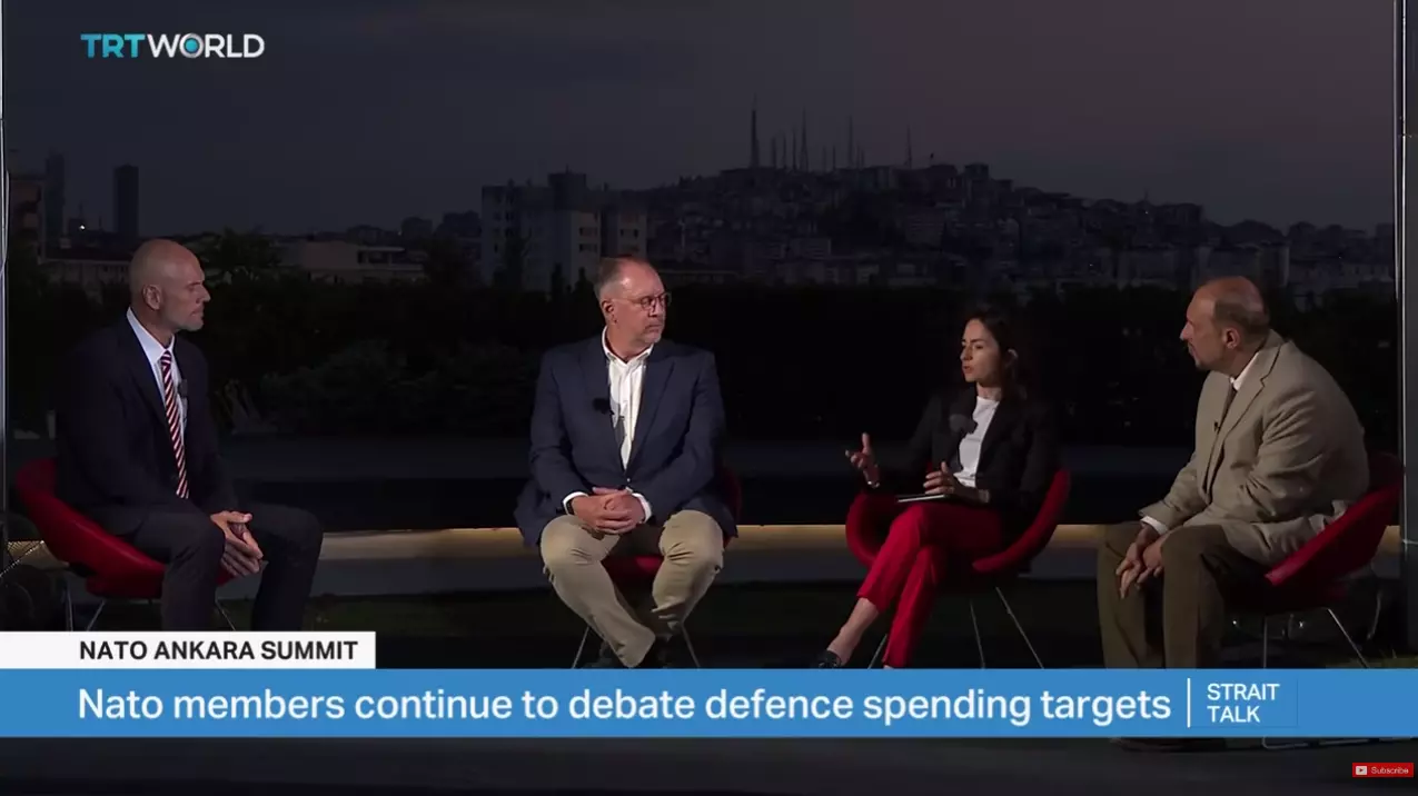 A wide shot of a four-person panel discussion on TRT World's Strait Talk broadcast during the NATO Ankara Summit. The group is seated outdoors at night with a city skyline in the background, and the on-screen graphic reads "Nato members continue to debate defence spending targets."