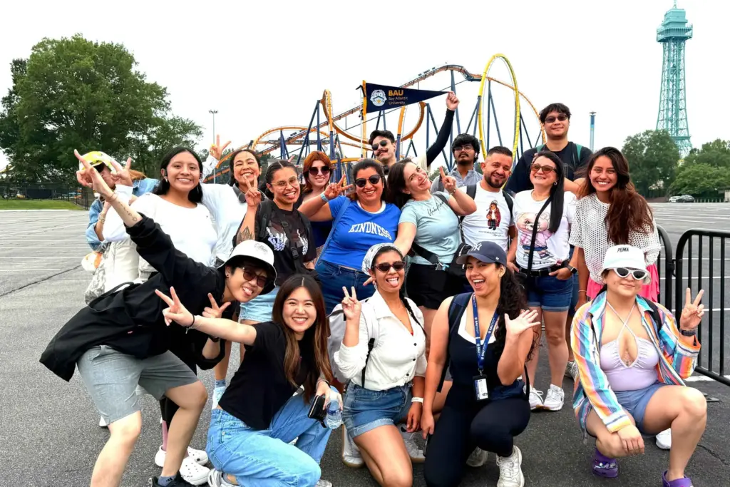 Smiling group at amusement park with roller coaster and flag, enjoying a fun and lively day outdoors.
