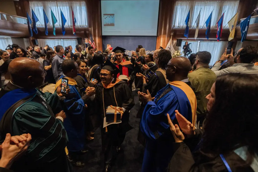 Graduation ceremony with graduates celebrating and receiving applause in an auditorium.