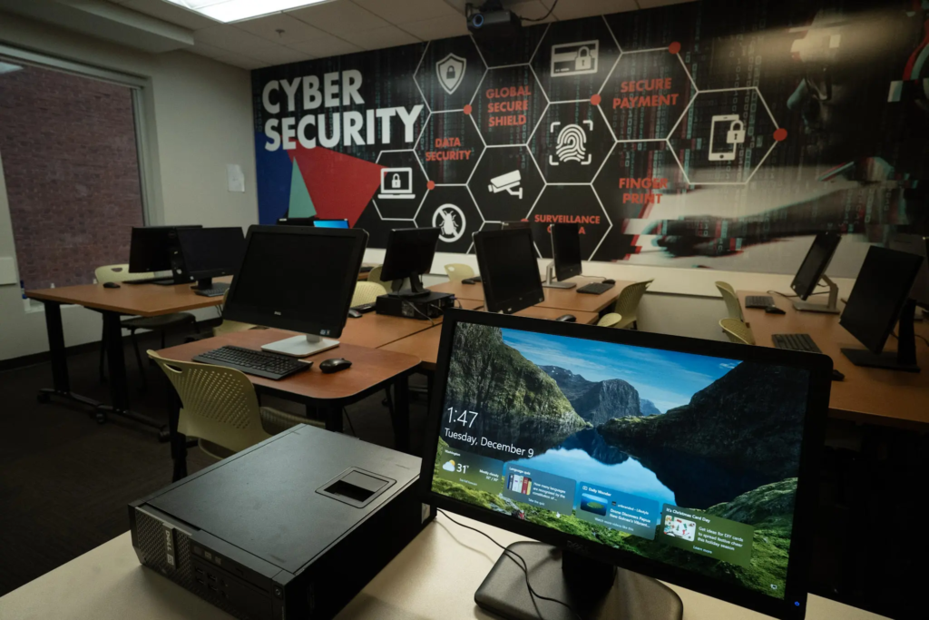 DSC02397 Cybersecurity classroom with computers and a digital security-themed mural covering the back wall.