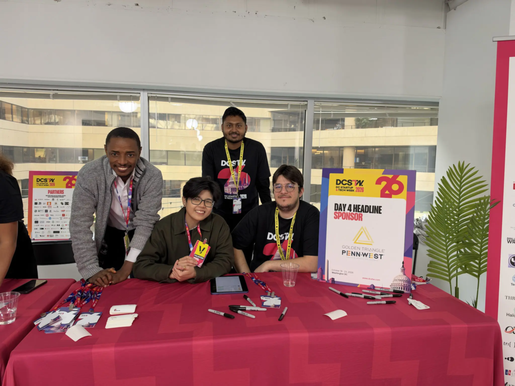 Group of people at a tech event table with sponsor signs and promotional materials.