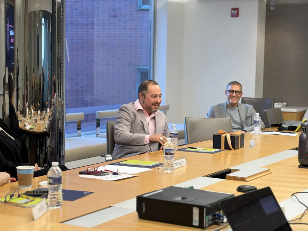 Business meeting with three professionals smiling around a conference table, gift box and documents on the table.