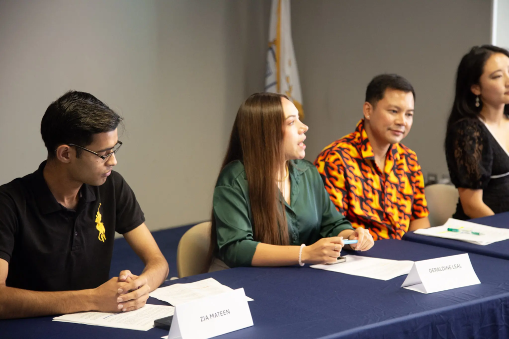 Four people in a panel discussion sit at a table with name tags, engaged in conversation.