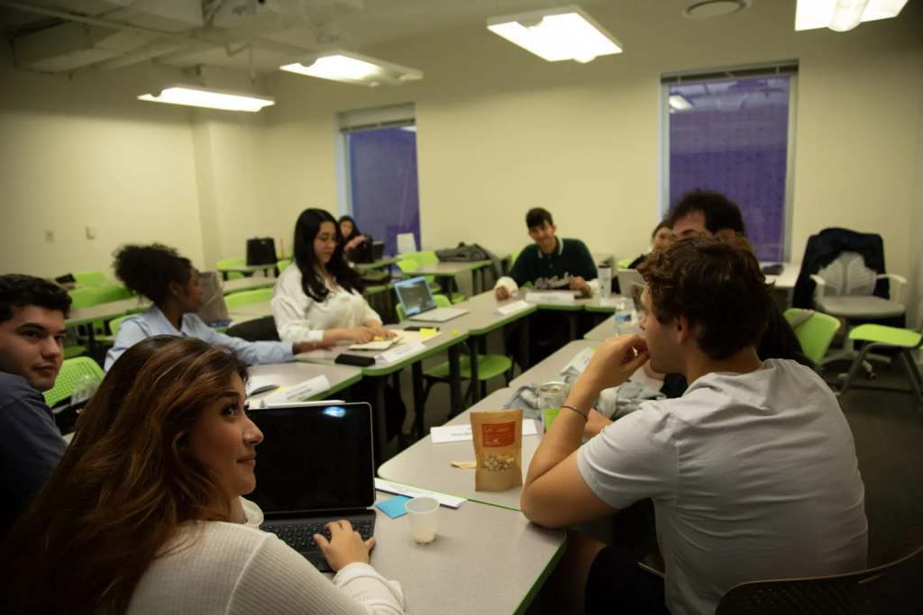 KQ9A3838 People collaborating in a modern classroom, engaging in discussion and using laptops for a group project.
