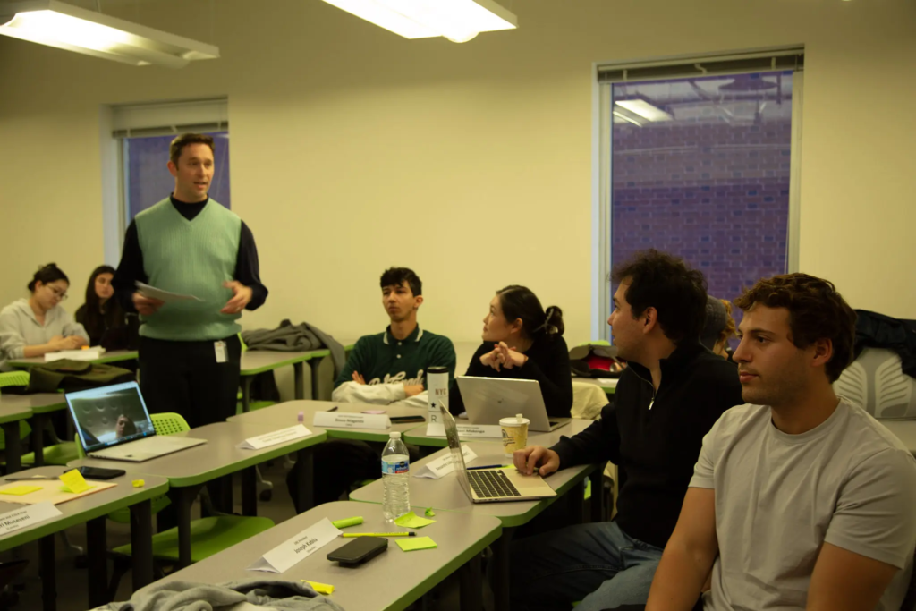 KQ9A3846 Instructor leading classroom discussion with students engaged and laptops open in a modern learning environment.