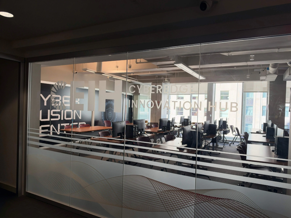 Untitled design (2) Modern office workspace inside Cyber Innovation Hub with computers and desks visible through glass walls.